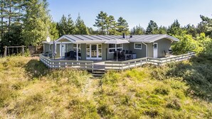 Et moderne hus med en overdækket terrasse, store vinduer og en træterrasse.
