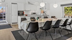 Moderni keittiö, jossa on valkoiset kaapit, keskellä oleva saareke tuoleineen ja riippuvalaisimet.