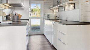 Een moderne keuken met witte kastjes, een ingebouwde oven, een koffieapparaat en een raam met uitzicht op een tuin.