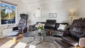 Een moderne woonkamer met een leren bank, een ronde salontafel en een groot raam met uitzicht op het omliggende landschap.