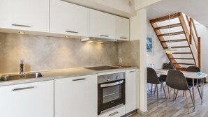 A modern kitchen with white cabinets, a stainless steel sink, and an oven. There is a dining area with a wooden table and chairs. - "Arna" - 2.3km from the sea by Interhome (Rømø)