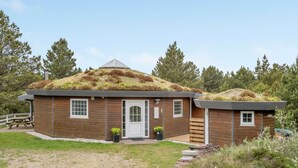 Een houten chalet met een gazondak, een voordeur en een klein portaal met bloempotten.