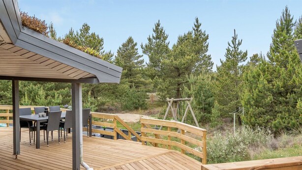 Een houten terras met tuinmeubilair, een schommel en uitzicht op bomen.