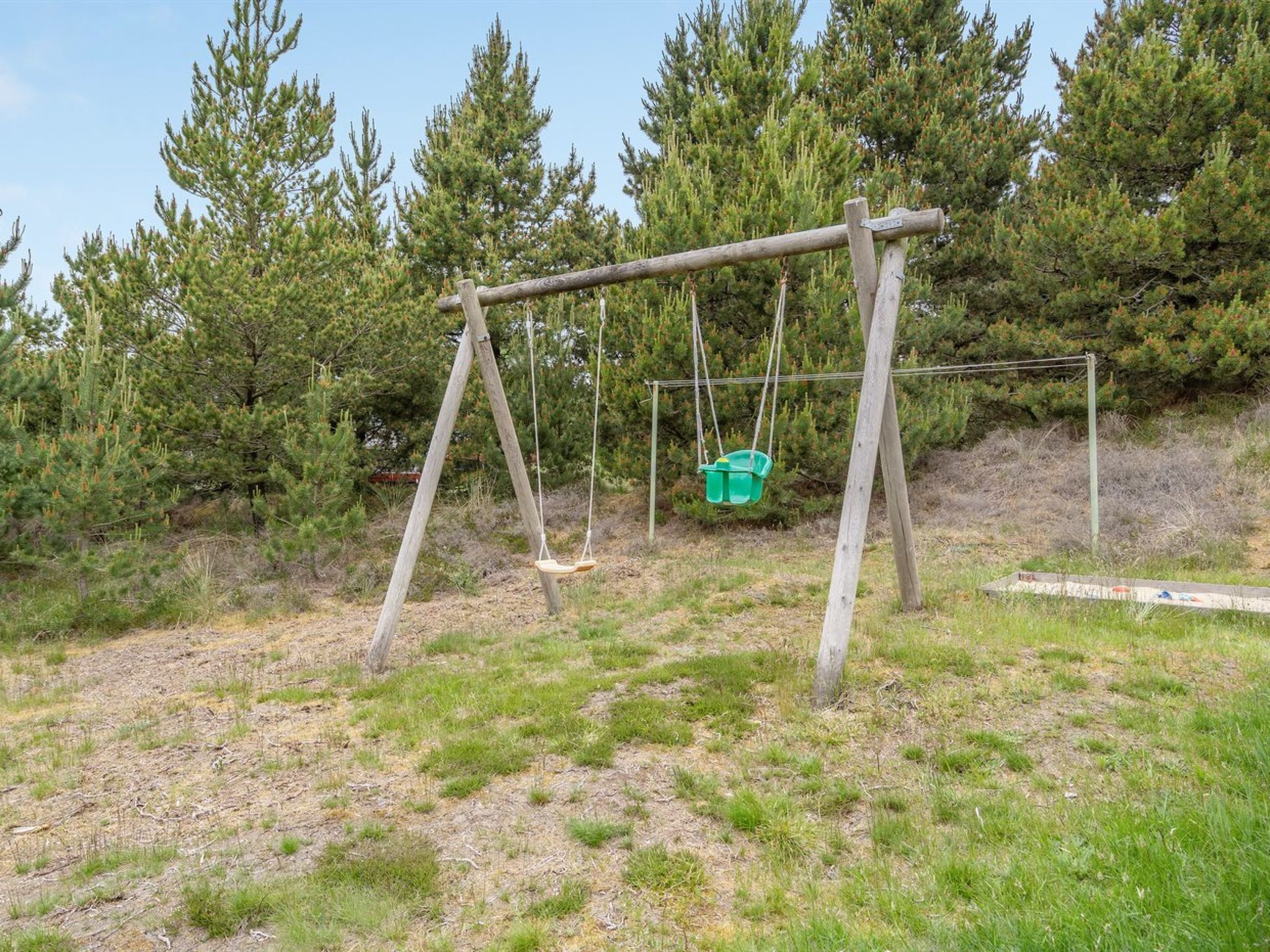 A wooden swing set in a grassy area with trees in the background.