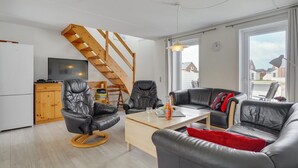 Uma sala de estar moderna com escada de madeira, móveis de couro, televisão de tela plana e grandes janelas com vista para o bairro.