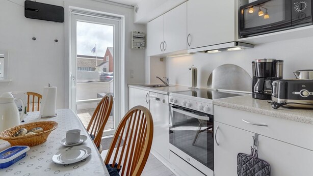 Uma cozinha moderna com armários brancos, forno embutido, micro-ondas e máquina de café.