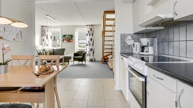 Une cuisine moderne avec des meubles blancs, une cuisinière et une machine à café. On y trouve également un coin repas avec une table et des chaises.