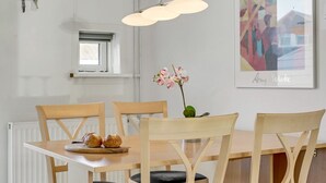 Un espace repas comprenant une table, des chaises, un luminaire suspendu, une fenêtre et une œuvre d’art encadrée.