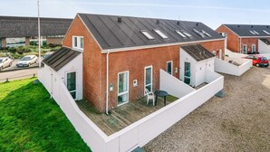 Un immeuble résidentiel moderne doté d’un toit en pente, de nombreuses fenêtres et d’un espace extérieur couvert comprenant une table et des chaises.