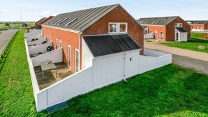 Un immeuble résidentiel moderne doté d’un toit en pente, d’un espace extérieur couvert avec des sièges et d’une pelouse bien entretenue.