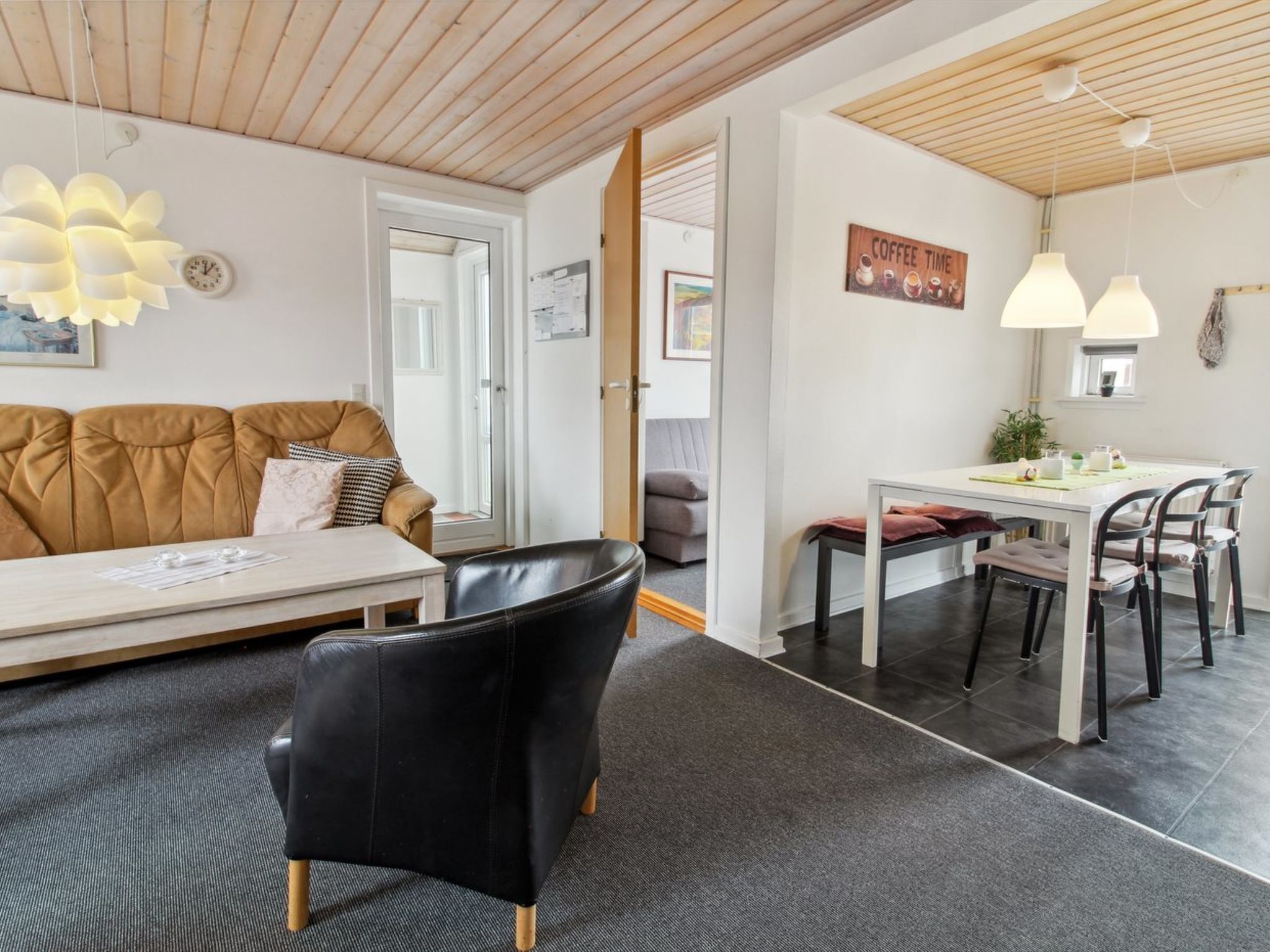 Un salon moderne avec un canapé, un fauteuil en cuir noir, une table à manger avec des chaises et un panneau décoratif représentant une tasse de café au mur.