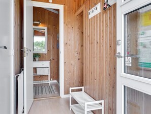 A wooden interior with a white bench, a small table, and a window with a view of greenery.