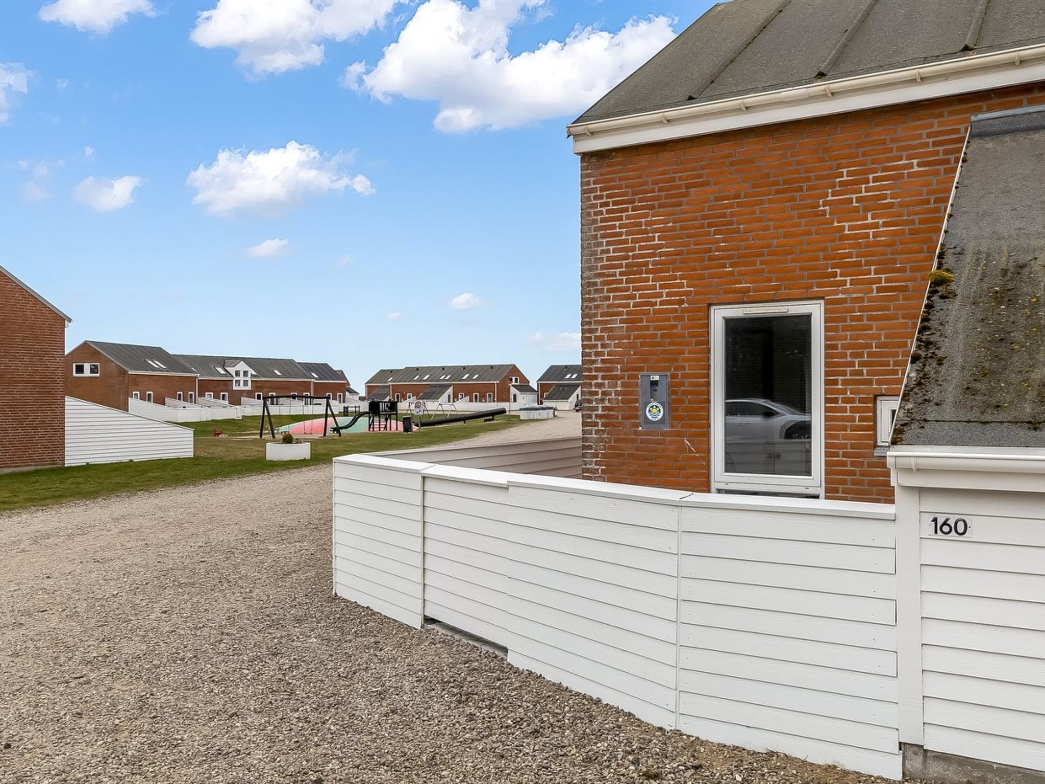 A row of brick houses with a gravel driveway and a fenced playground area.