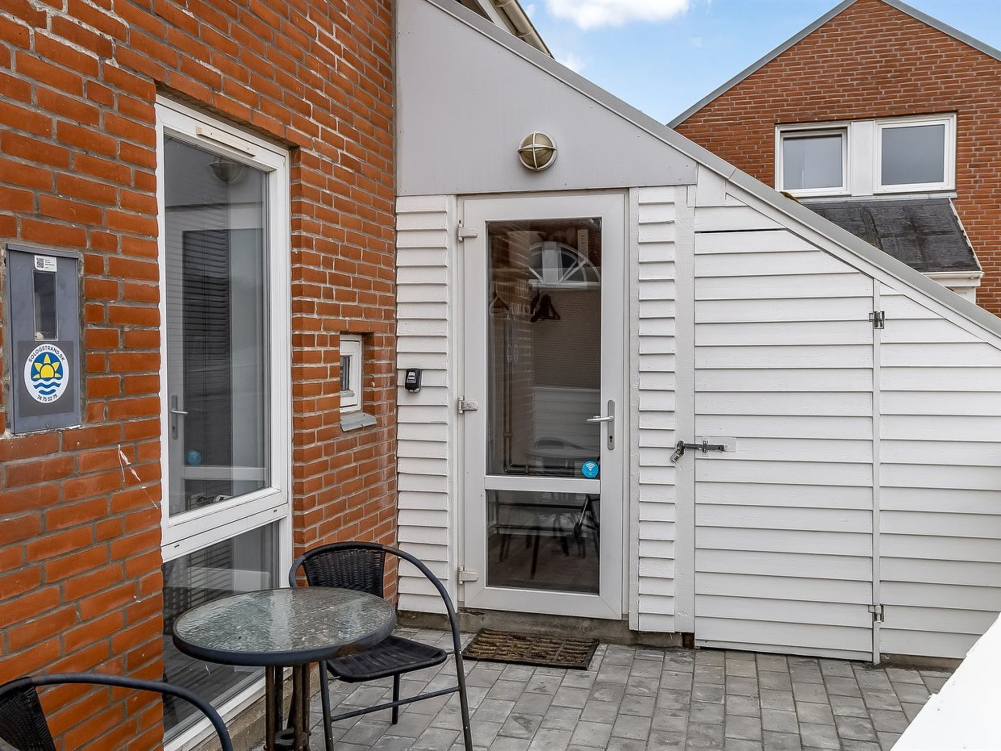 Een terras met een glazen deur naar een kamer, een tafeltje met stoelen, en een bakstenen muur.