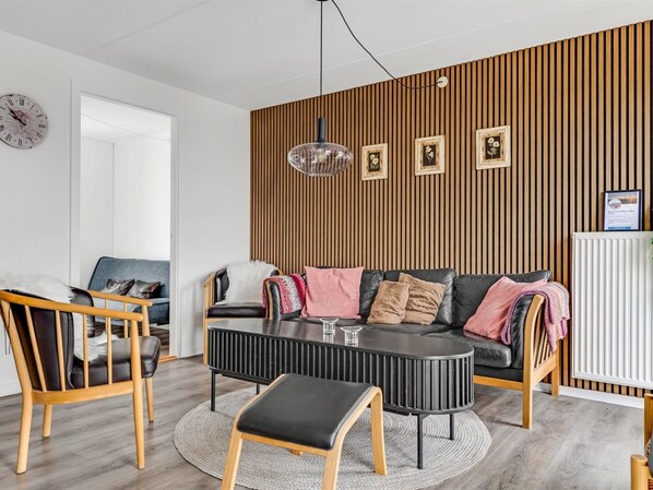 A modern living room with a wooden slat wall, a round coffee table, a sofa with cushions, a dining area with a chair, and a wall clock.