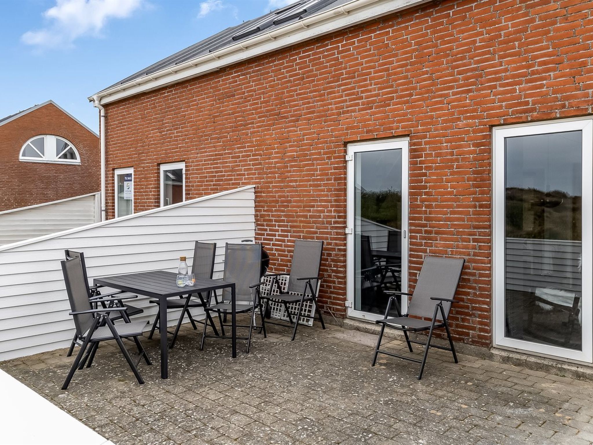 Eine Terrasse mit Tisch und Stühlen, eine Glasschiebetür und ein Backsteinhaus.