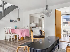 A modern living space with a dining area, kitchen, staircase, and a view through an open door.
