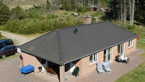 Ein eingeschossiges Backsteingebäude mit flachem Dach, einer überdachten Terrasse mit Gartenmöbeln und einer kleinen Garage.