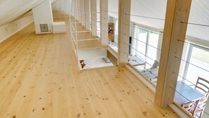 Ein geräumiges Dachzimmer mit Holzdielen, einer Treppe und großen Fenstern mit Blick ins Freie.