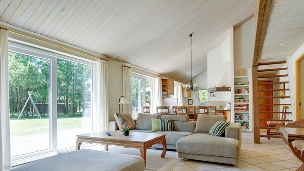 Ein geräumiges Wohnzimmer mit großem Fenster, einer Sofagarnitur, einem Couchtisch und einem Essbereich mit Stühlen und Tisch.