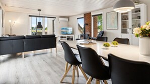 Ett modernt vardagsrum med en svart soffa, ett matbord med stolar, en tv och en öppen spis.