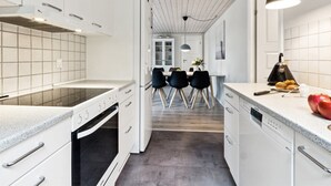 Ett modernt kök med vita skåp, en svart ugn och en matplats med ett bord och stolar.