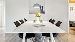 Ett modernt matrum med ett vitt bord, svarta stolar, en hängande lampa och en inramad tavla ovanför bordet.