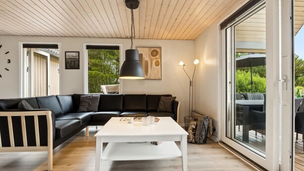 Ett modernt vardagsrum med en svart lädersoffa, ett vitt soffbord och ett stort fönster med utsikt över grönområden.