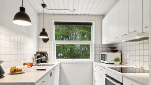 Ett modernt kök med vita skåp, en inbyggd ugn, en mikrovågsugn och ett fönster med utsikt över träd.