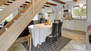 Een eethoek met een tafel voor vier personen, een keuken op de achtergrond en een houten trap.