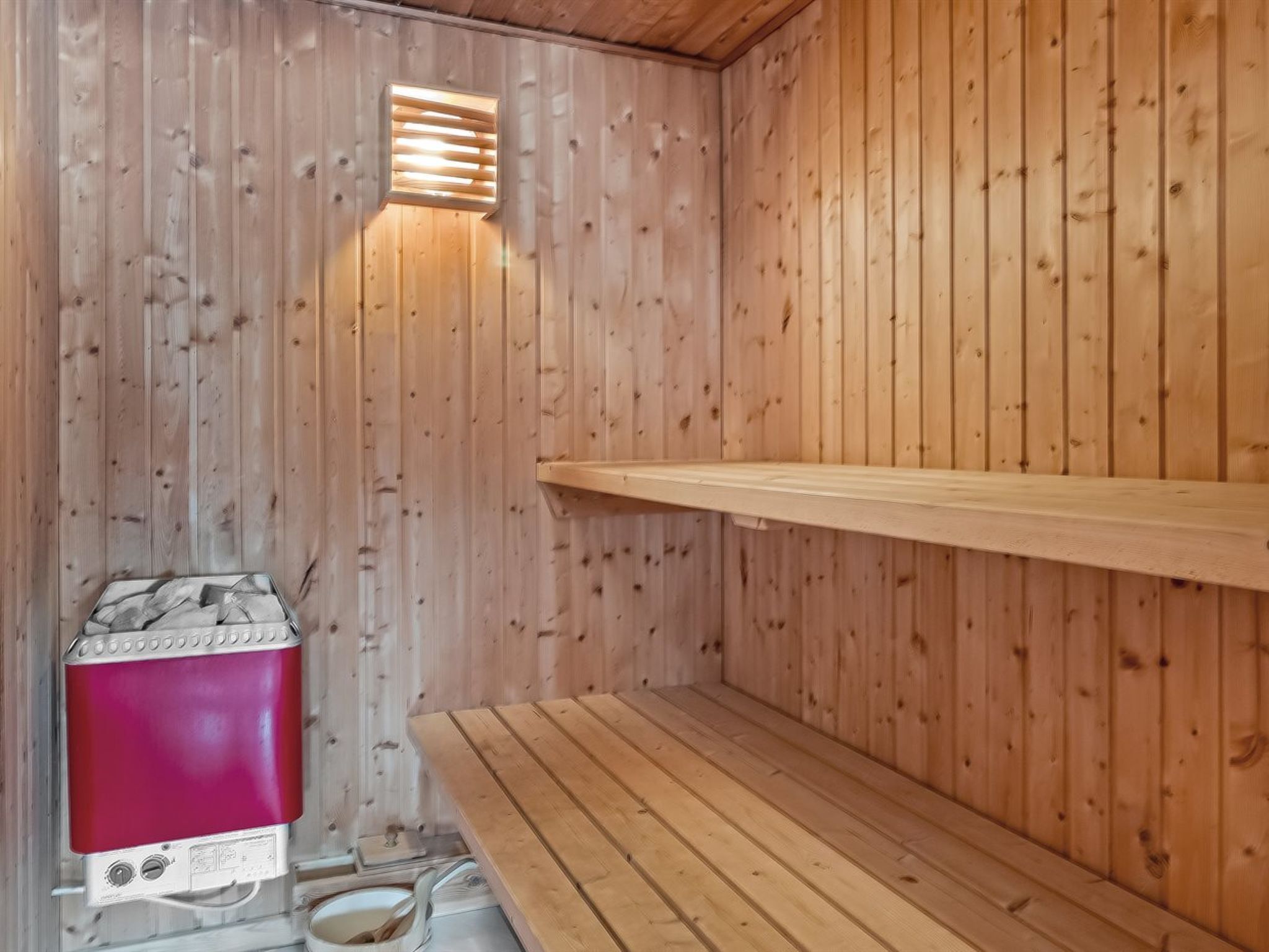 Un sauna avec des murs en bois, un banc et un appareil de chauffage rouge.