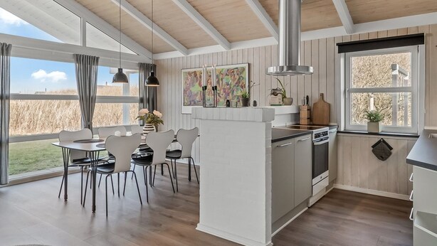 Une cuisine moderne dotée d’un îlot central, de grandes fenêtres et d’un coin repas avec des chaises et une table.
