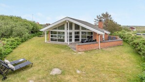 Une maison moderne avec une grande façade vitrée, une extension en briques et une cour gazonnée.