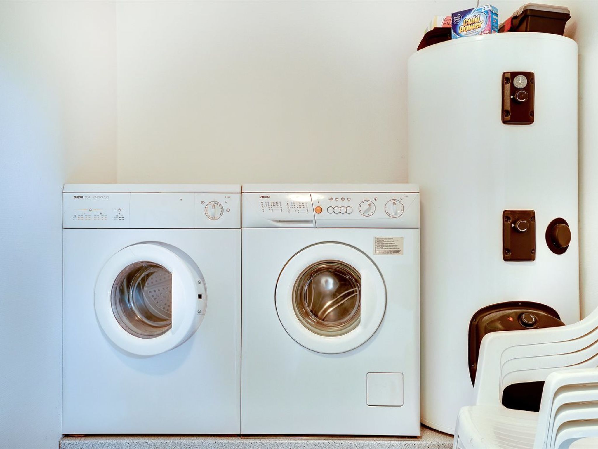 A laundry area with two front-loading washing machines and a tall white cabinet with a control panel.