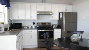 A modern kitchen with white cabinets, stainless steel appliances, a black countertop, and a dining table with chairs. - Great little getaway  (Port Hastings)