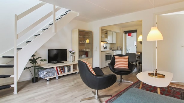 Un salon moderne avec un escalier, un téléviseur à écran plat, un coin repas et une cuisine.