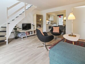 Ein modernes Wohnzimmer mit Treppe, Flachbildfernseher, Essbereich und Küche.