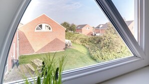 Une vue à travers une fenêtre donnant sur un quartier résidentiel, avec des maisons en briques, une pelouse et un ciel dégagé.