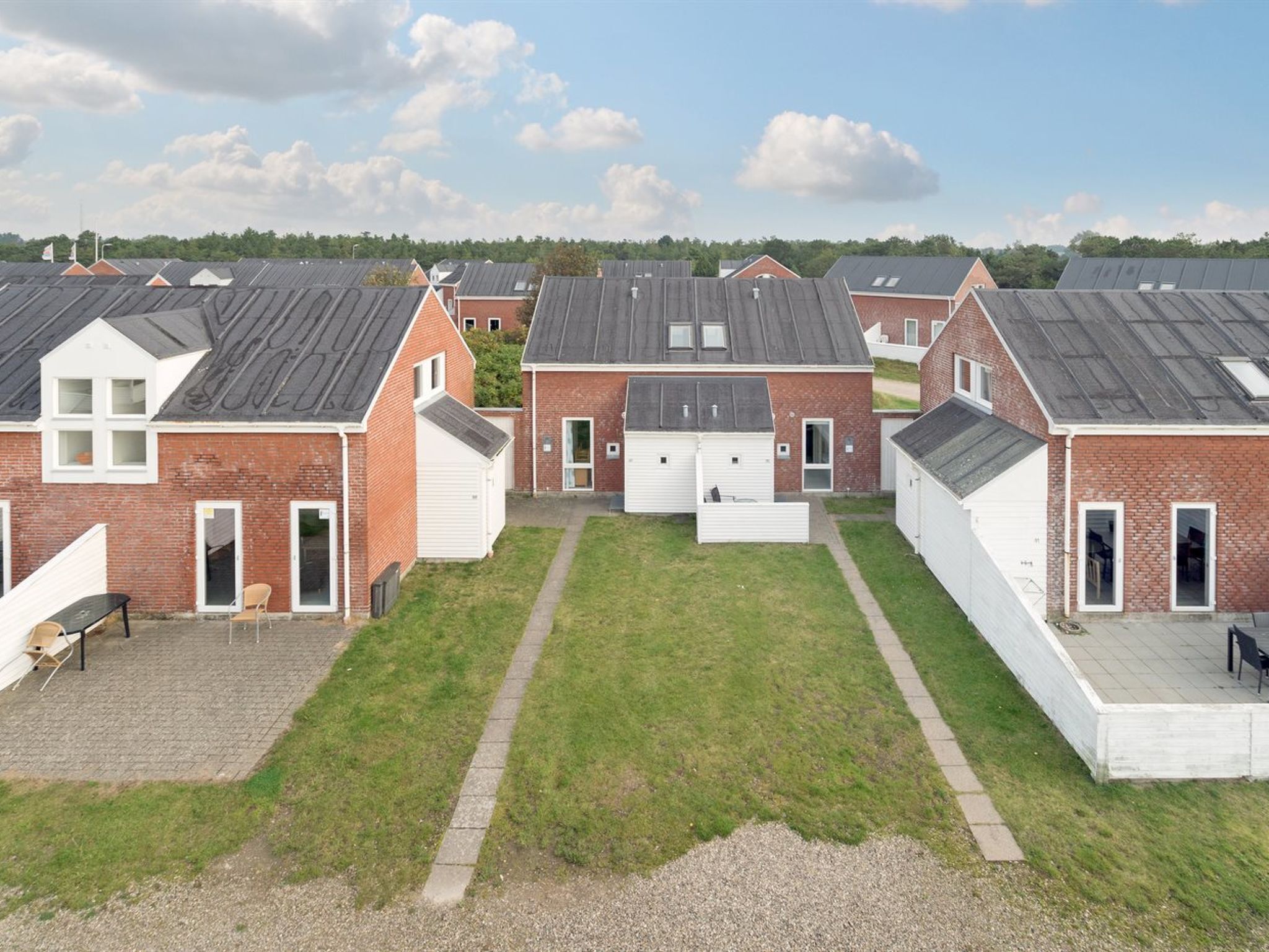 Eine Reihe von Backsteinhäusern mit flachen Dächern und weißen Garagentüren, angeordnet in einem Innenhof mit einer Rasenfläche und Kieswegen.