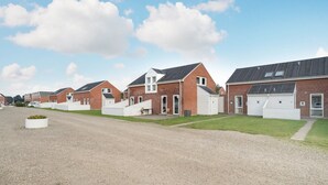 Une rangée de maisons modernes en briques, dotées de garages attenants, d’une allée en gravier et d’un espace verdoyant agrémenté d’un parterre de fleurs.