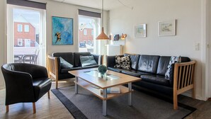 A modern living room with a black leather sofa, a wooden coffee table, and a black armchair. There are two windows with blinds, a painting on the wall, and a radiator. - "Mahena" - 2.3km from the sea by Interhome (Rømø)