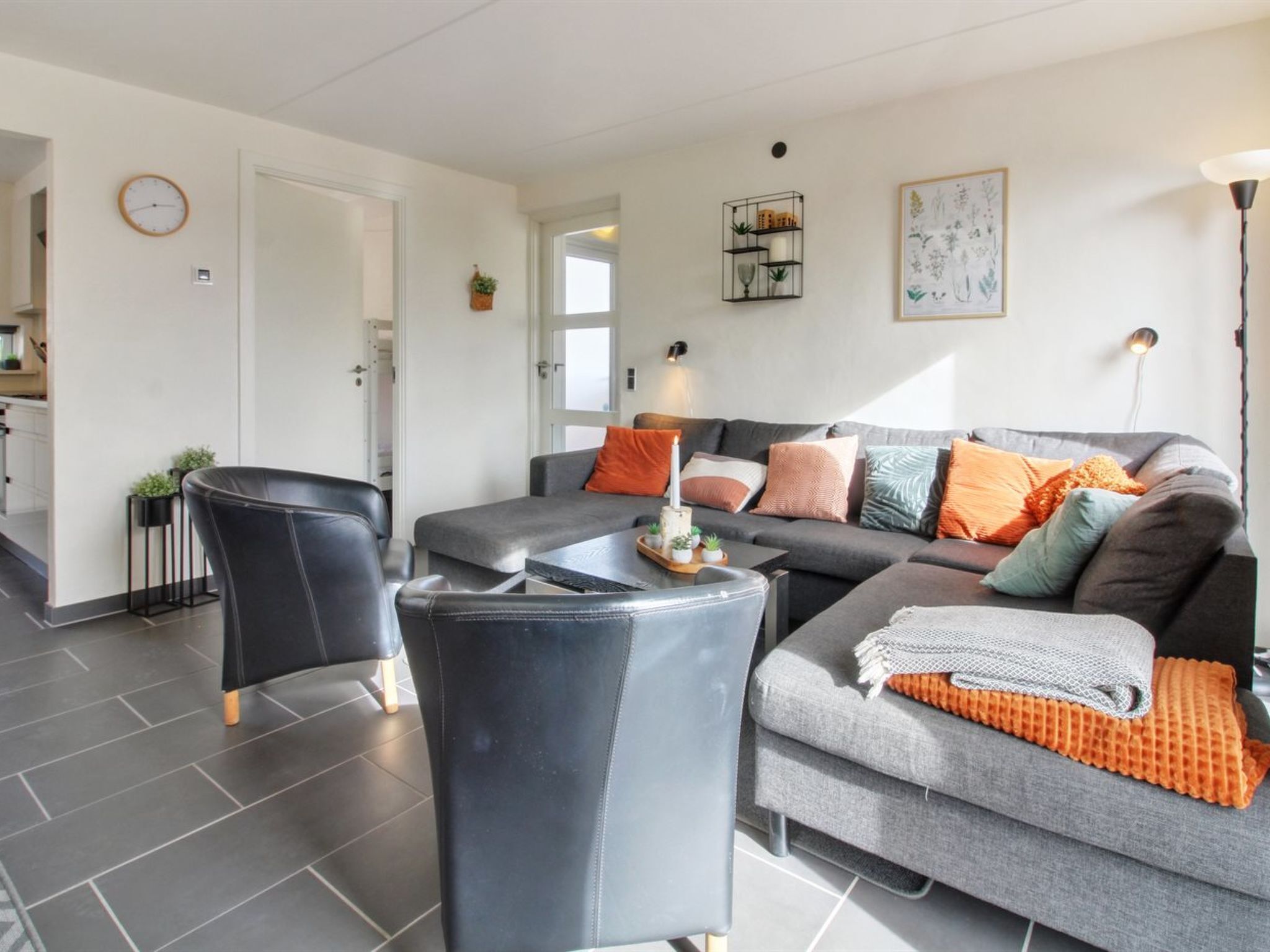 Een moderne woonkamer met een bank, fauteuil en salontafel, een keuken met kasten, en een eettafel.