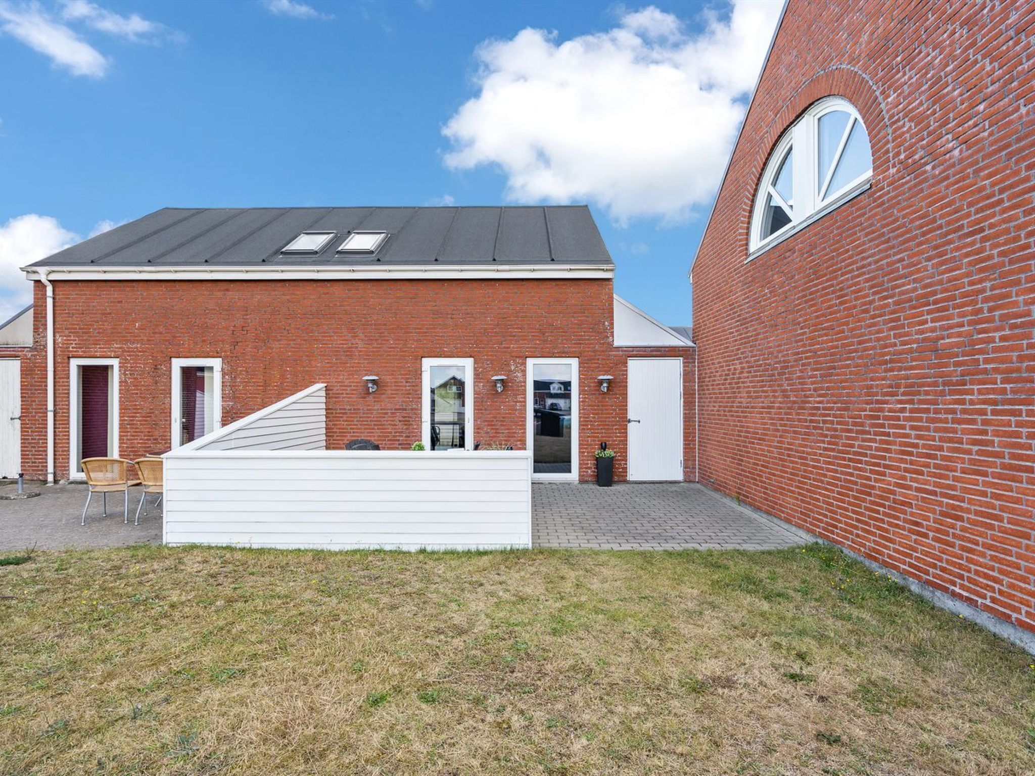 Een gebouw van rode baksteen met een plat dak, een witte deur en een klein overdekt gedeelte met stoelen.