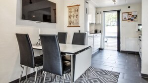 Een moderne eetruimte met een tafel en stoelen, een wandgemonteerde televisie en een keuken met kasten en een raam.
