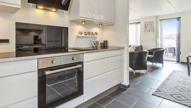 Een moderne keuken met een inbouwoven, een eethoek met een tafel en stoelen, en uitzicht buiten door een glazen deur.