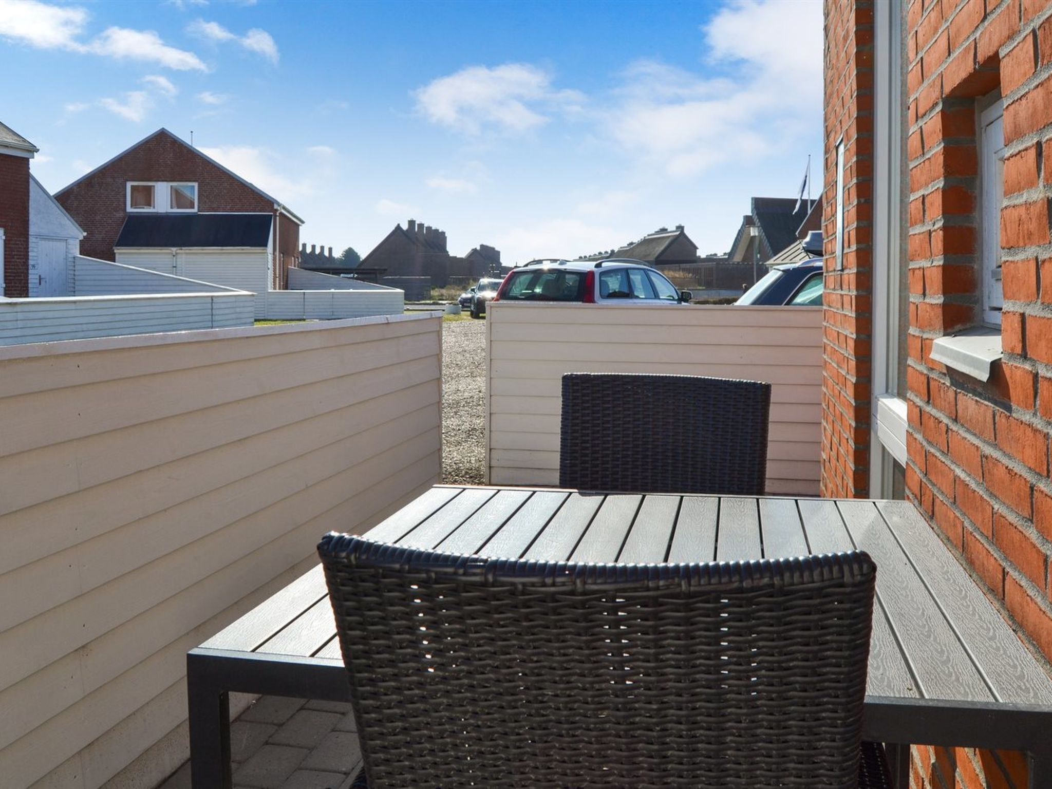 Eine Terrassenfläche mit Tisch und Korbstuhl, umgeben von einer niedrigen Mauer, unter klarem Himmel.