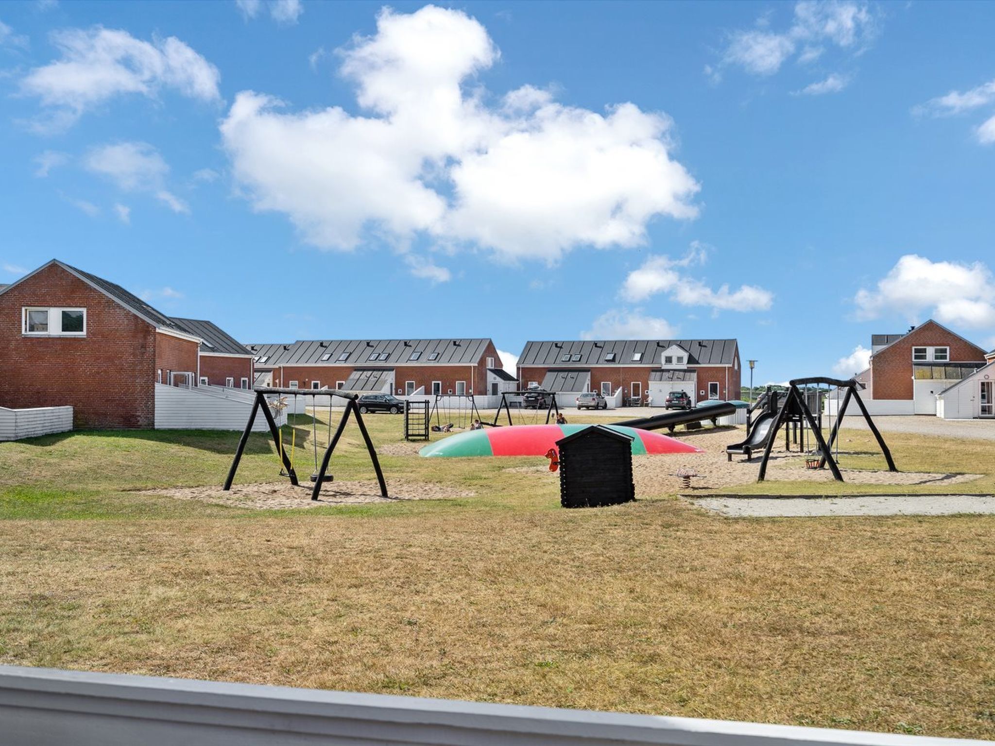 Un patio de juegos con columpios y toboganes, rodeado de edificios con fachadas de ladrillo y techos inclinados.