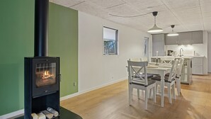 Una sala moderna con estufa de leña, un comedor con mesa y sillas, y una cocina con alacenas y un lavamanos.