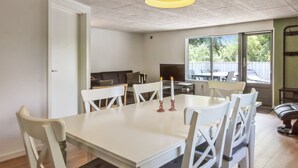 Un comedor con una mesa y sillas blancas, un sofá y un televisor al fondo.