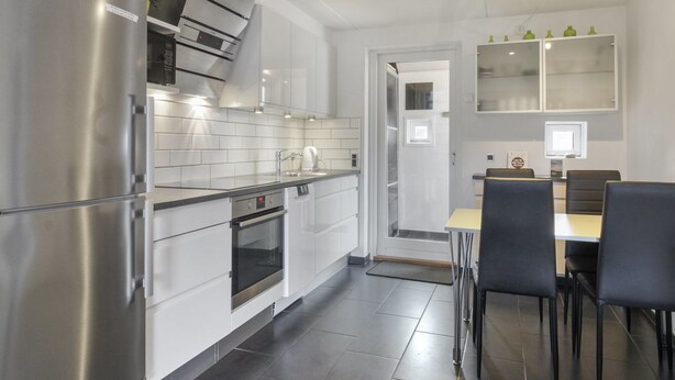 Una cocina moderna con electrodomésticos de acero inoxidable, armarios blancos y un comedor con sillas negras.